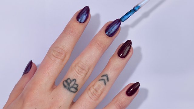 Close-up of a light skin hand with tattoos to which a second layer of nail polish is being applied