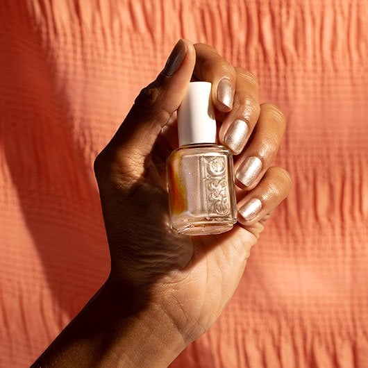 dark skin model holding a bottle of it's all bright metallic champagne polish and wearing it