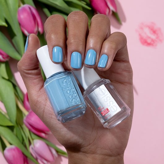 Dark skin hand palming a bottle of tu-lips touch blue nail polish and a bottle of clear topcoat" (Default Alternate Text: "Dark skin hand palming a bottle of tu-lips touch blue nail polish and a bottle of clear topcoat