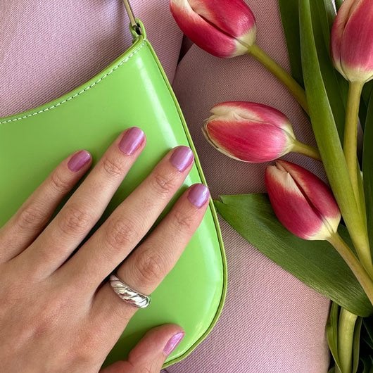 Flirty flutters nail polish on a light skin hand resting on a lime green handbag near pink tulips