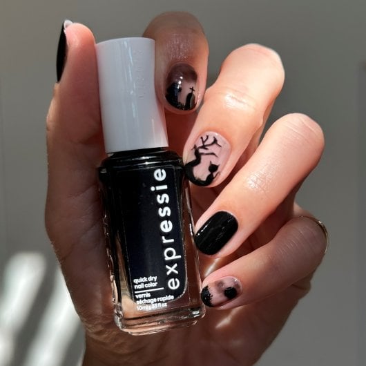 light skin hand with spooky cat nail art holding black nail polish bottle