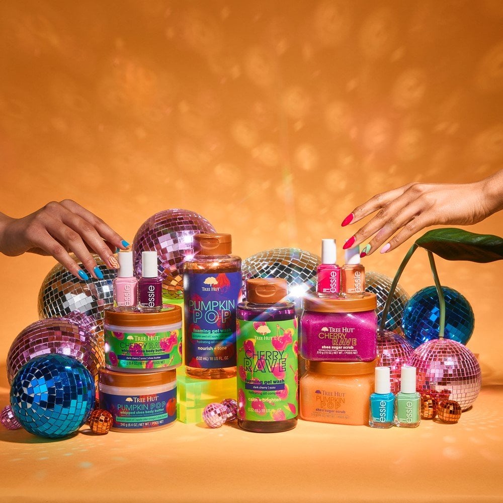 two hands reaching out for essie nail polish bottles resting on Tree Hut skin care products with disco balls and an orange background