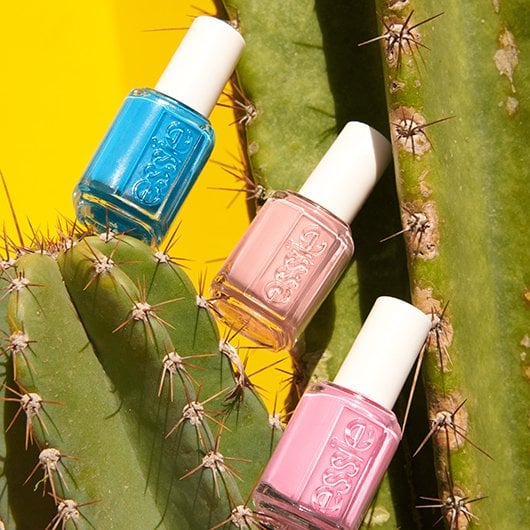 Three bottles of pink and blue essie nail polish balanced on a cactus against a yellow background