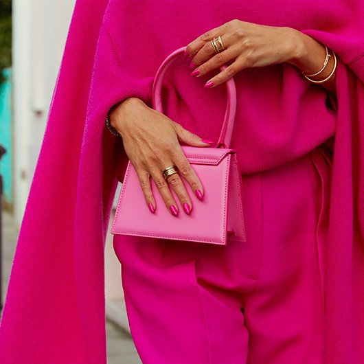 Woman dressed in bright pink formal clothing holding a pink purse with a pink colored manicure