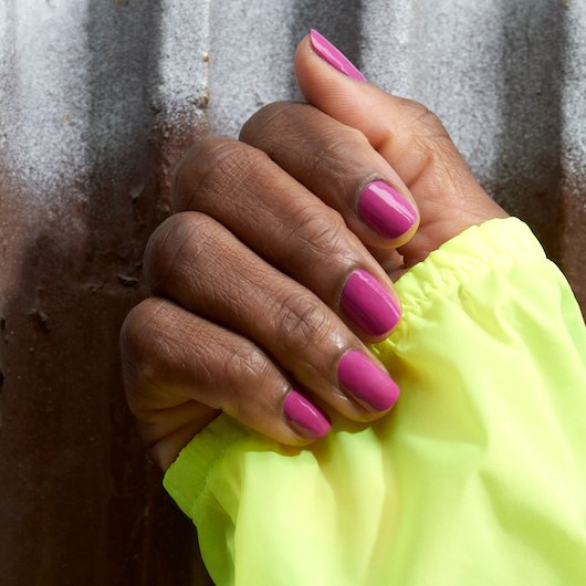 Medium skin hand wearing dark pink essie nail polish folded over clutching a yellow sleeve cuff