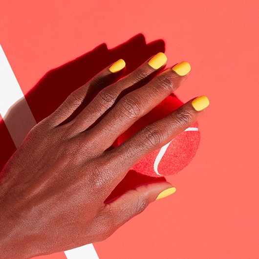 Hand with nails painted in the shade sunshine be mine hovering above a red tennis ball on a tennis court background