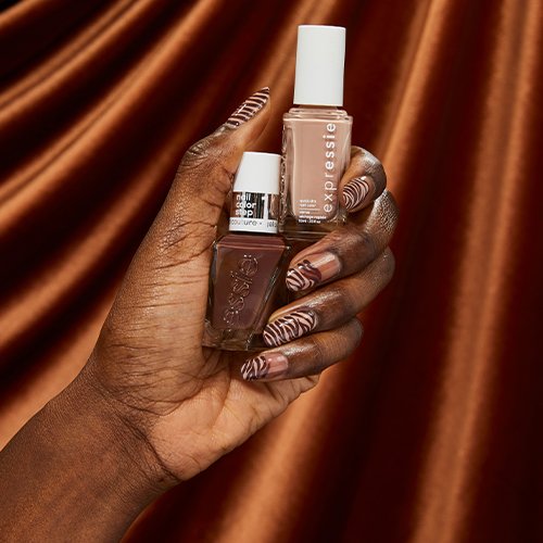hand with zebra stripe nail art holding two bottles of brown essie nail polish