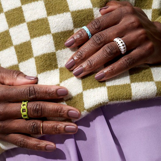 Dark skin model wearing colorful clothing showing fingernails painted in a neutral skin tone shade