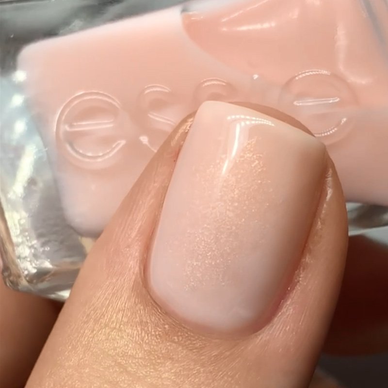 Nail painted with light pink shimmery polish with a bottle of essie nail polish in the background