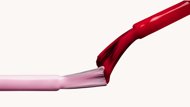 Lavender and red nail polish brushes touching on a white backdrop