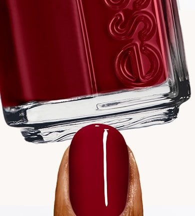Nail painted with bordeaux nail polish under an Essie dark red nail polish bottle