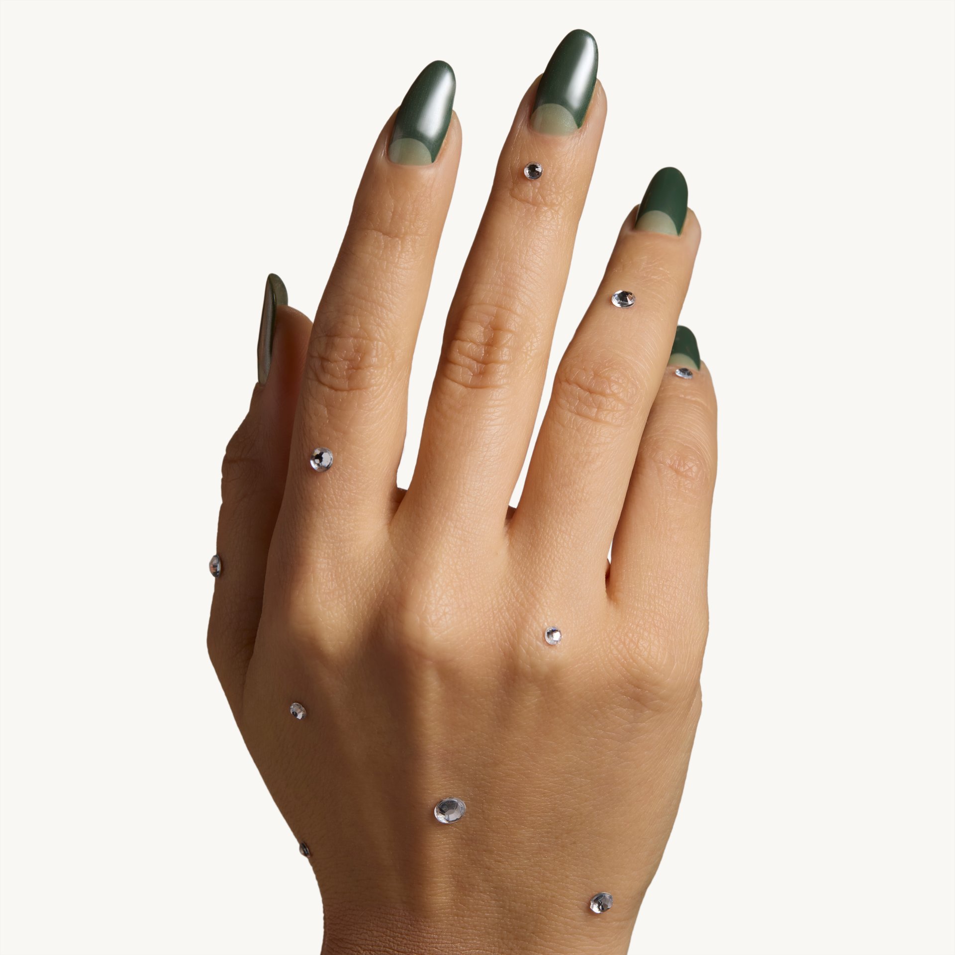 A hand featuring dark green nails with a half-moon design, accented by small crystals scattered across the skin.