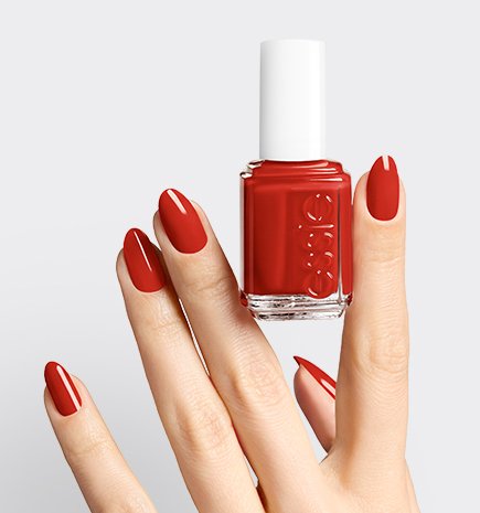  A hand with long, oval-shaped red nails holding a bottle of "Forever Yummy" essie nail polish.