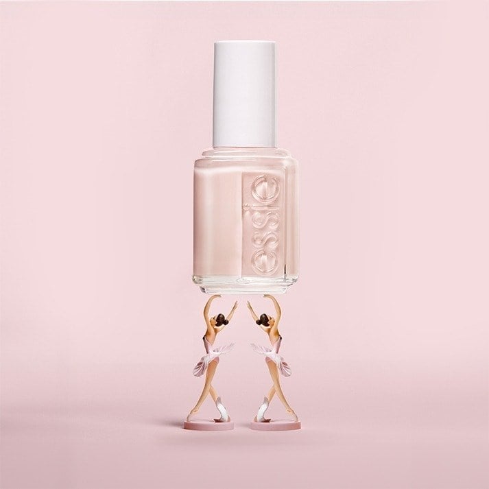 essie Ballet Slippers nail polish creative ad featuring a large sheer pink polish bottle supported by two miniature ballerinas on a monochromatic pink background.