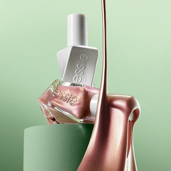 Shiny pink nail polish pours beside two essie nail polish bottles resting on a green pedestal against a soft green backdrop