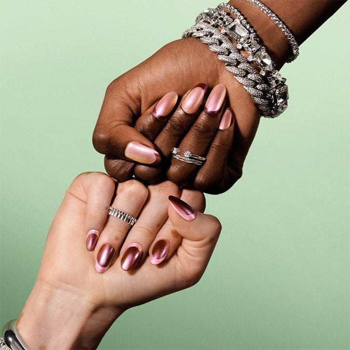 Stacked fists on pale green; almond nails feature iridescent pink and metallic copper French tip designs with silver jewelry.