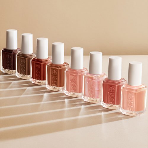 Seven nail polish bottles in shades ranging from dark brown to light pink are lined up on a beige surface.
