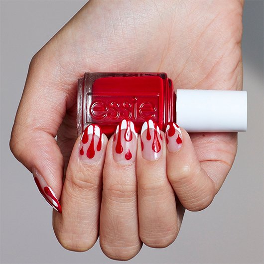 light skin hand featuring vampire nail art holding a bottle of red-y for bed essie nail polish