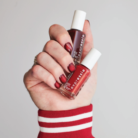 light skin hand featuring vampy vampire nail art holding two bottles of expressie nail polish