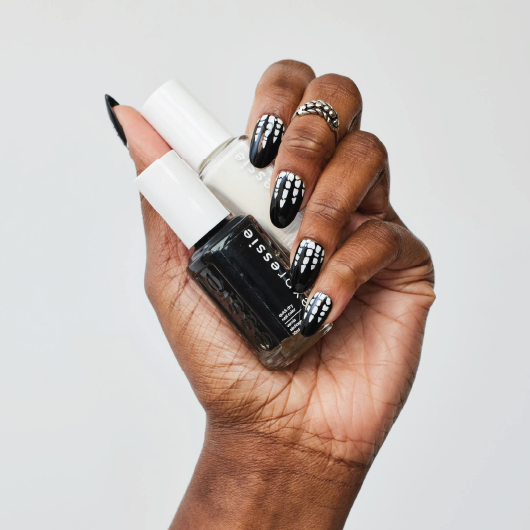 dark skin hand featuring spooky skeleton nail art holding two bottles of expressie nail polish