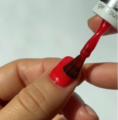 A close-up of a person using a brush to apply vibrant red nail polish to their fingernails