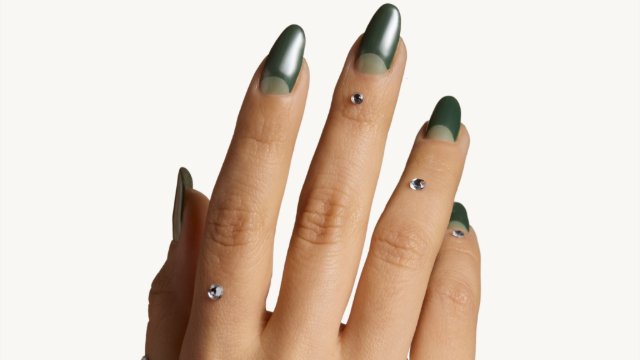 A close-up of a woman's hand with green nails adorned with a sparkles