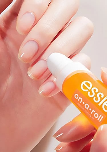 a light skin hand with nude nails getting essie on a roll cuticle oil applied on three nails