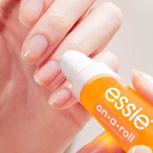 closeup of essie on a roll cuticle oil being applied to nude nails on a light skin hand