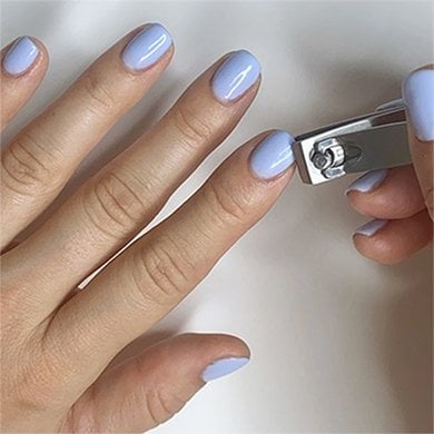 a nail clipper trimming the index fingernail on a light skin hand wearing light blue polish