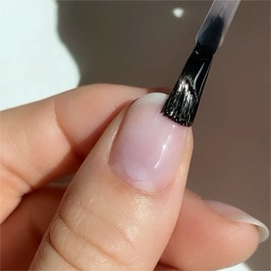 closeup of clear nail strengthener being brushed on the thumbnail of a light skin hand