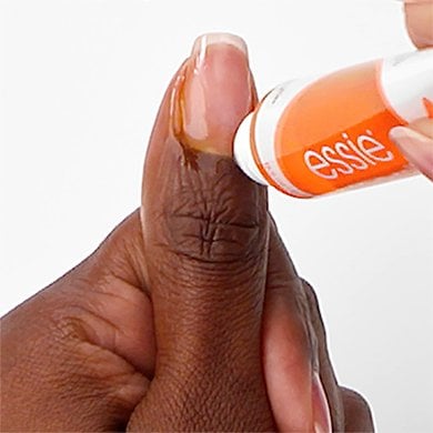 closeup of the thumb on a dark skin hand while essie cuticle oil is being applied