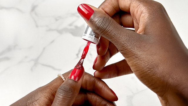 Dark skin hands painting a thumbnail with red essie longwear gel nail polish
