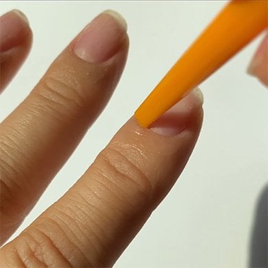 Light skin hand with cuticles of index finger being pushed back with a plastic orange pusher