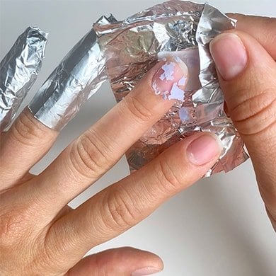 A foil wrap being removed, showing gel polish dissolved into large flakes and coming off
