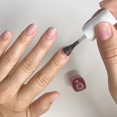 Light skin hands applying hard to resist nail strengthener to the index fingernail.