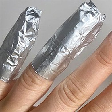 Closeup of a light skin hand, pinky and ring finger with tips wrapped in tin foil.
