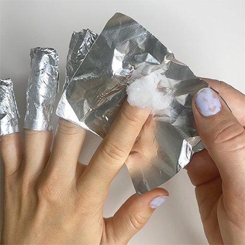 Light skin hands, one with 3 fingertips wrapped in foil, the 4th being wrapped over a cotton ball.