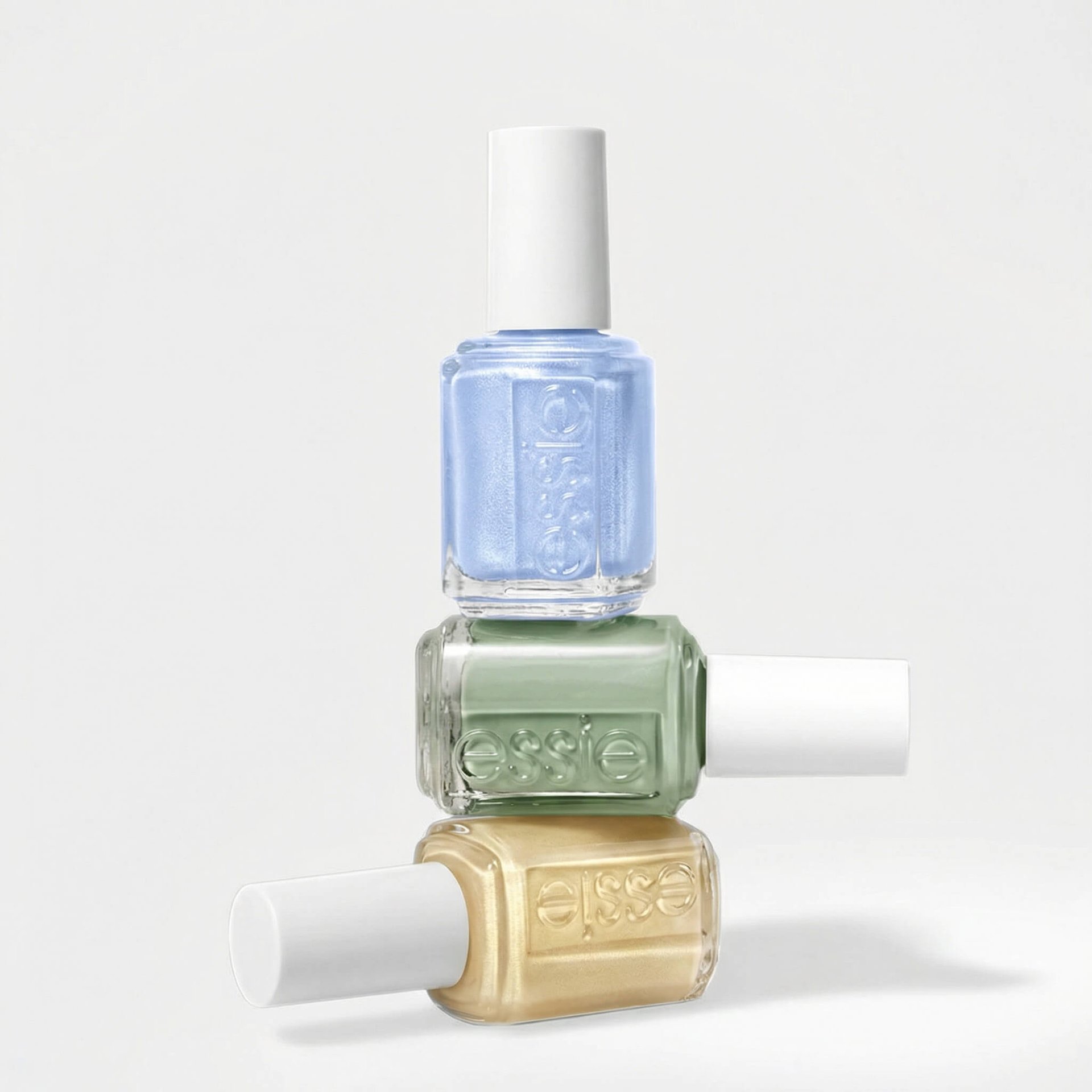 White background with three bottles of essie pastel nail polish piled on top of each other