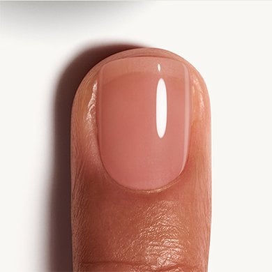 medium skin fingernail against white background wearing a nude pink essie nail polish