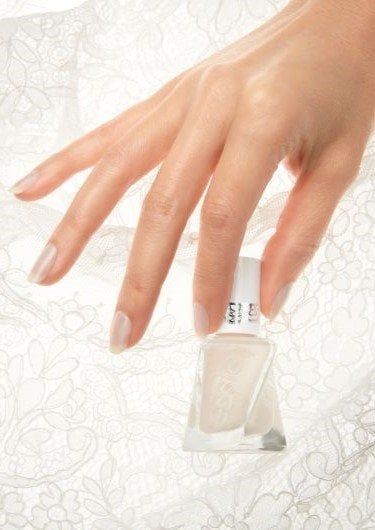 a hand with sheer white painted nails holding a soft white bottle of essie gel couture nail polish with a lace background