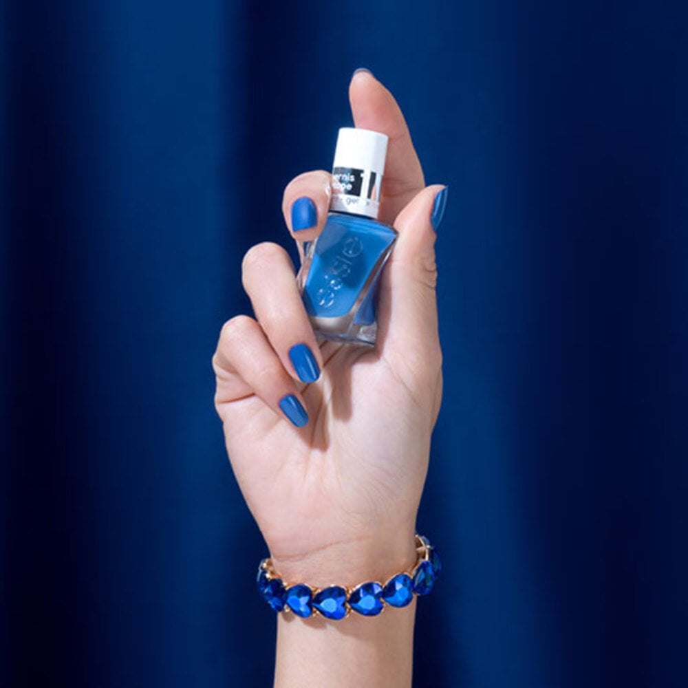 a hand with blue painted nails holding a royal blue bottle of essie gel couture nail polish