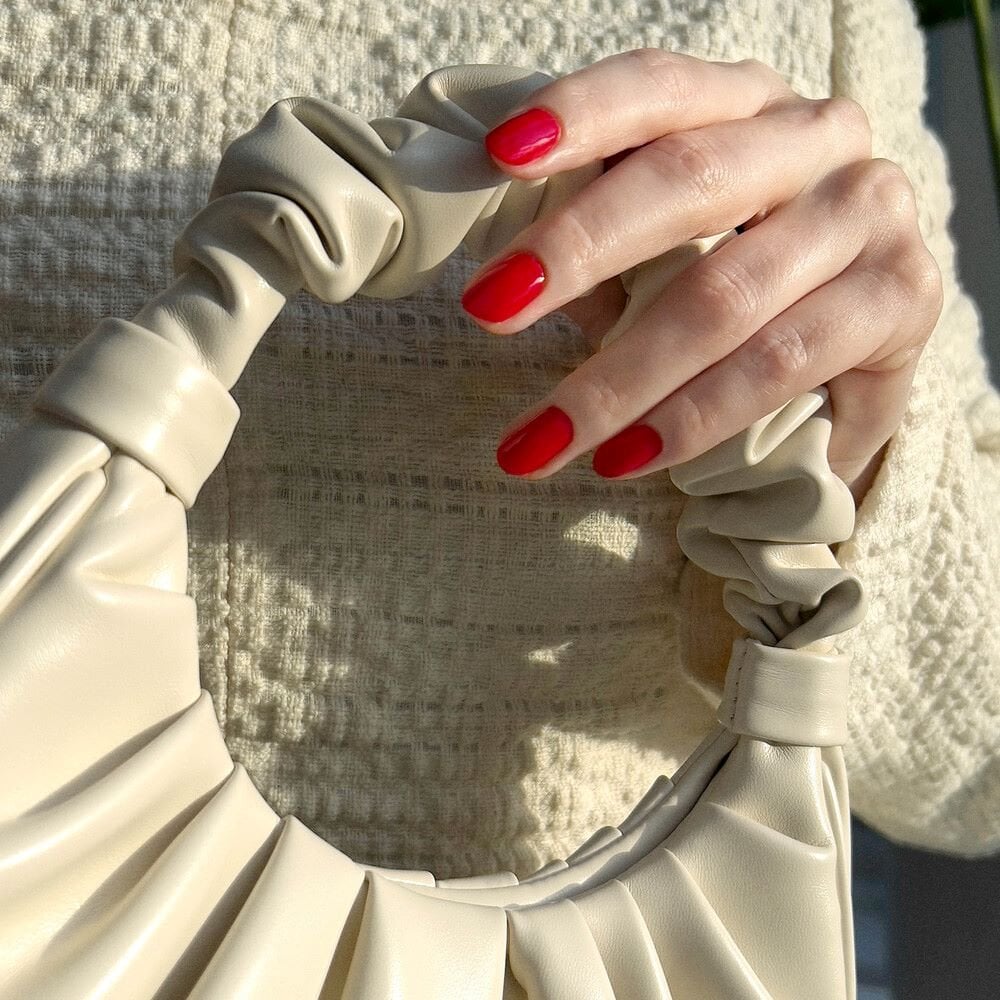 a hand with red painted nails holding a white handbag from the handle