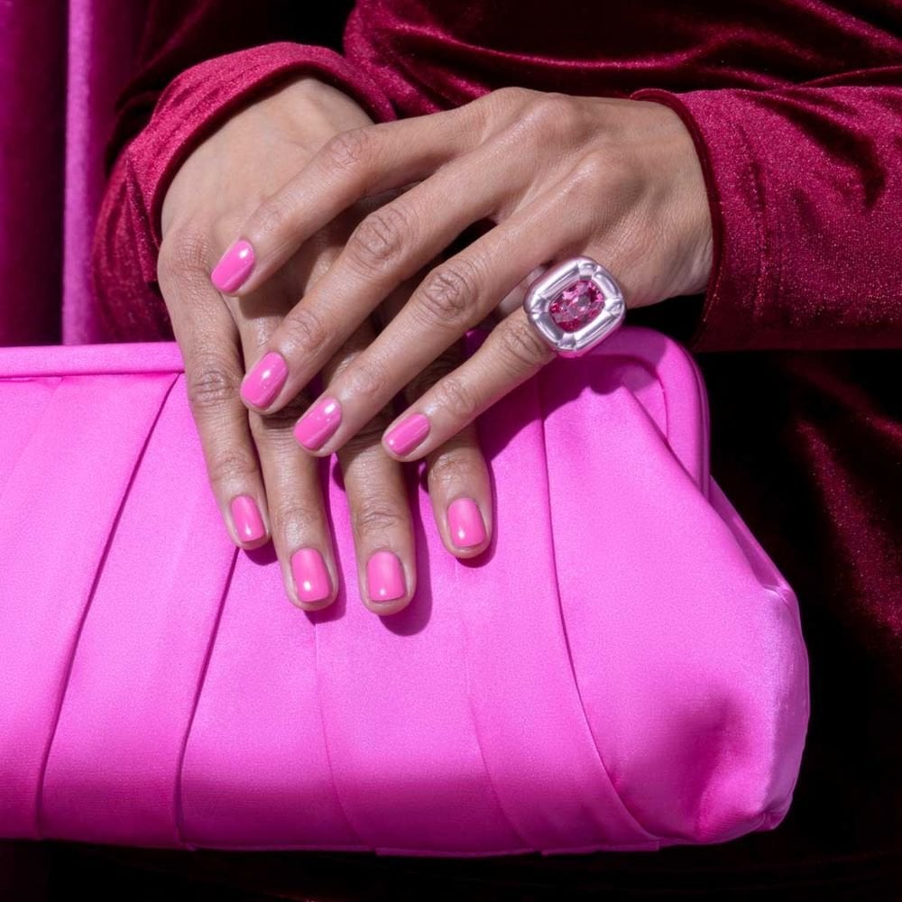 a hand holding a pink clutch purse with bright pink painted nails and a pinky ring