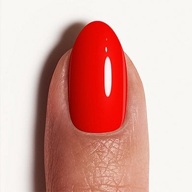 Closeup of a light skin fingertip wearing red-orange 'geranium' essie nail polish