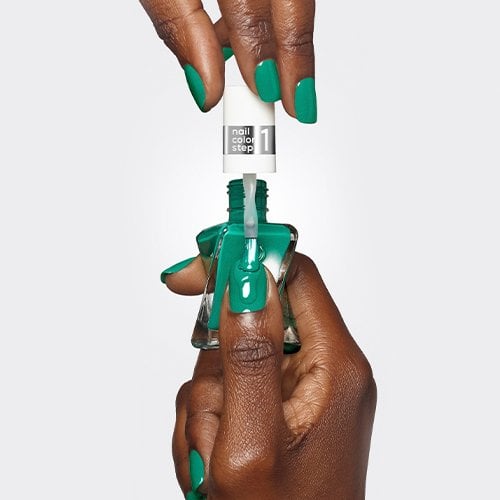 Dark skin, open bottle of vibrant green nail polish, brush dipped.  Step 1 label visible.