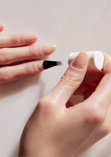 Light skin hand with bottle of clear nail treatment brushing it on the index finger of other hand