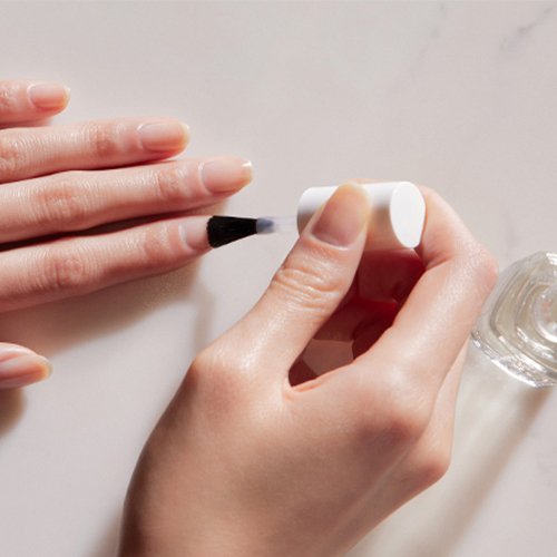 A bottle of clear nail treatment near light skin hand brushing some on the other hand