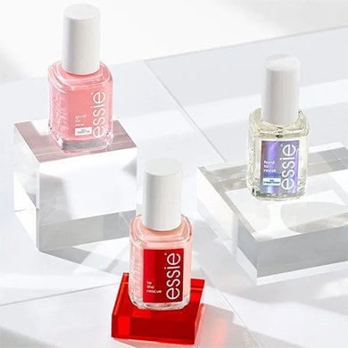 Lineup of essie nail treatments on red background, dark skin hand reaching down touching one
