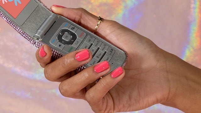 Medium skin hand wearing pink essie nail polish holding an open gray flip phone