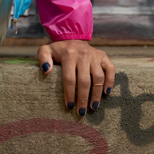 Medium skin hand wearing dark blue polish resting on the edge of a concrete stair with graffiti